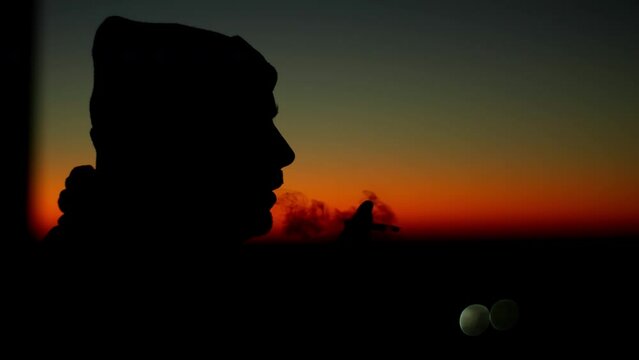 Close-up of a guy smoking a cigarette and blowing smoke. Silhouette of a man at sunset. Harmful habits that harm health. High quality 4k footage