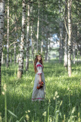 Girl in a wreath of flowers in a birch forest with a jug in her hand