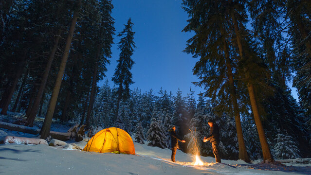 couple camping with campfire and tent outdoors in winter forest