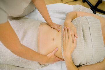 Crop masseuse massaging tummy of woman