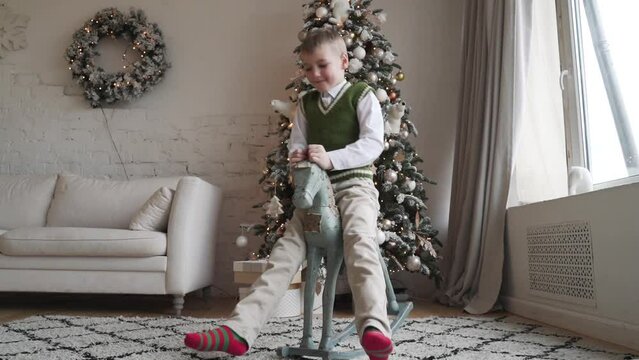 a little white boy in a green Christmas sweater on a toy rocking horse 