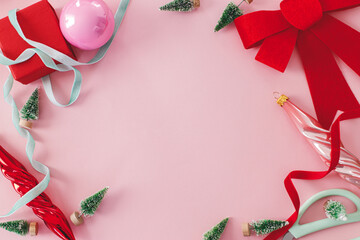 Pink Christmas. Modern Christmas flat lay with red bow, baubles, little green trees and ribbons on pink background. Creative christmas background with space for text, seasons greetings. © sonyachny