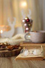 Fototapeta na wymiar Cup of tea or coffee, various sweets and spices, Christmas decorations, comfy blanket, books and glasses. Selective focus.