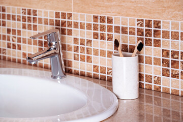 Luxury faucet mixer and wooden toothbrushes on a white sink in a beautiful bathroom. 