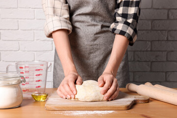 Woman kneading dough at wooden table near white brick wall, closeup