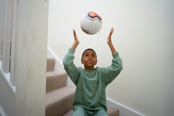 Boy sitting on stairs and throwing soccer ball in air