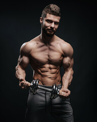 Fototapeta na wymiar Muscular hunk with dumbbell posing in studio. Fitness male model holding gym equipment. Shirtless man at black background.