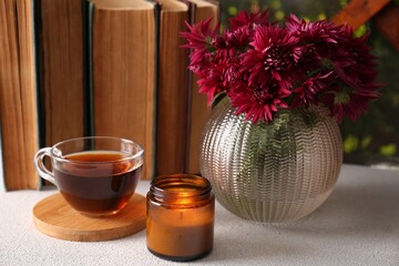Beautiful pink chrysanthemum flowers, candle and cup of aromatic tea on light grey table