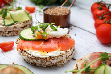 Crunchy buckwheat cakes with salmon, poached egg and microgreens on white wooden table, closeup