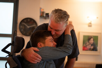 Father embracing disabled son at home