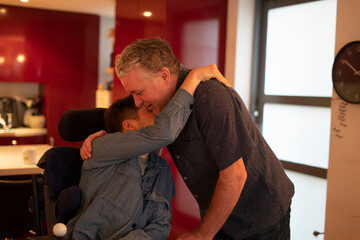 Father embracing disabled son at home