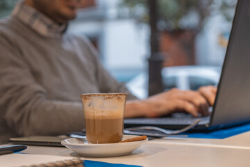 Empresario sentado en una cafetería, trabajando con su ordenador, tomando un café.