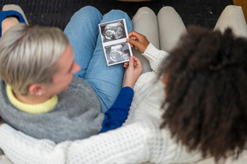 Overhead view of lesbian couple looking at baby ultrasound image  - Powered by Adobe