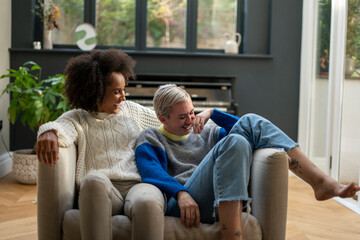 Smiling lesbian couple relaxing on armchair at home