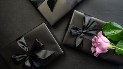 Gift box wrapped in black paper with a black bow on a dark background. Rose. Holiday concept. Black Friday.