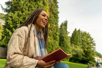 Smiling woman in coat holding book in park in autumn