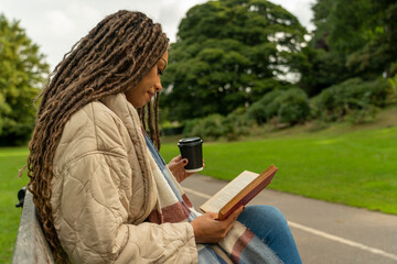 Woman in coat reading book in park in autumn