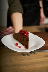 Woman with a passion for cooking decorates a slice of handmade chocolate cake in her home kitchen with blackberries and red currants.