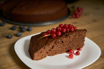 Handmade chocolate cake decorated with cranberries and red currants on the wooden kitchen table.