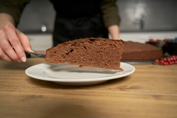 Woman with a passion for cooking decorates a slice of handmade chocolate cake in her home kitchen with blackberries and red currants.