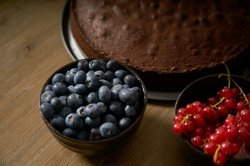 Handmade chocolate cake decorated with cranberries and red currants on the wooden kitchen table.