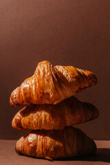 Three fresh and soft croissants on a brown background with room for text. Fresh crispy Creative design of bakery and fresh pastries