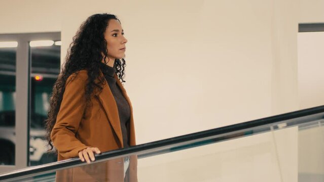 Side View Serious Caucasian Hispanic Lady Girl 30s Female Businesswoman Buyer In Shopping Center Mall Company Office Walking Indoors Standing On Escalator Woman Walks On Moving Staircase From Parking