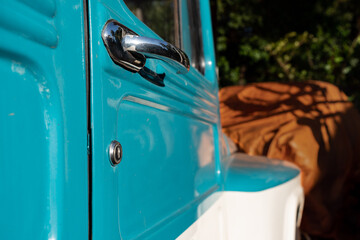 Detail of the chrome door handle of an ancient blue and white Rural Willis jeep car with a blurred background