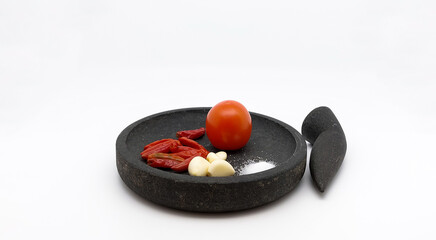 Red Chilies, Garlics, Tomato, and Salt on stone ware,  ingredients for making traditional Indonesian Sambal Tomat or Spicy Tomato Sauce. Isolated on white background. Side view.