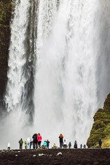Tourists standing under Skogafoss Waterfall - close up vertical shot