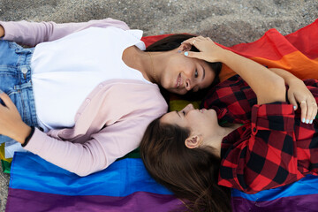  Beautiful lesbian young couple embraces and holds a rainbow flag. Girls enjoy at the beach.