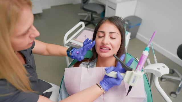 Woman Professional Dentist Performs Treatment Procedure on Female Patient in Modern Dental Clinic. Beautiful Orthodontist with Blond Hair Treats Client Teeth. Medicine and Healthcare. Slow motion