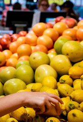 woman hand choosing lemon while shopping in supermarket.