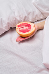 Woman is holding a grapefruit in bed. Female masturbation concept sexy fruit composition. Juicy fruit and vagina symbol