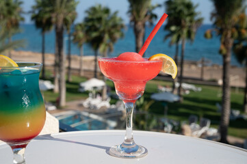 Colourful cold Strawberry daiquiri and Rainbow Paradise cocktails drinks served in glasses at outdoor cafe overlooking blue sea and palm trees, relax and holidays at sea