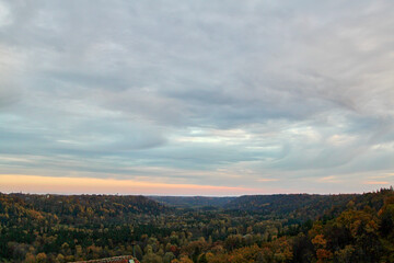A beautiful view on colourful autumn forest and cloudy sky with slight evening fog. Selective focus