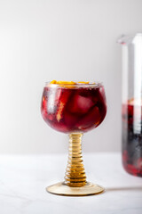 Glass of traditional red sangria with red wine, ice and fruits, light background