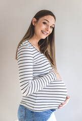 Obraz premium Portrait of a smiling pregnant woman against a white wall looking at camera.