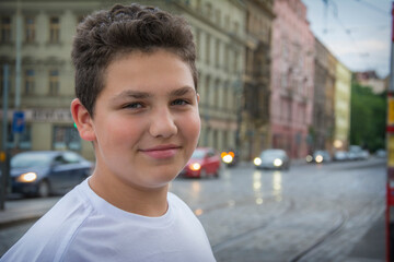 On a summer evening, a boy stands near the road in the city.