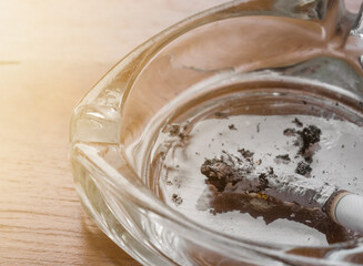 Close up cigarette put on ashtray with wooden table, light effect. Campaign to stop smoking concept.