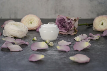              Natural homemade face cream in white packaging on grey marble background with dusty pink roses and rose petals.                   