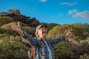 Cheerful senior caucasian woman with open arms in mountain trekking enjoying nature and freedom....