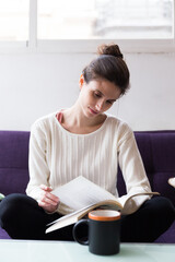 Woman sitting indoors on a sofa reading a book alone.