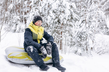 Fototapeta na wymiar Portrait of teenage boy sitting on tubing winter snowy forest. Child walking resting relaxing contemplating thinking daydreaming outdoors. Teen deep in thought