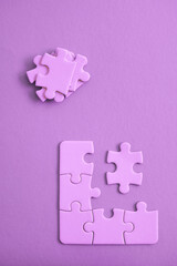 Purple jigsaw puzzle pieces on purple backgroun with pieces piled and ready to be fit.