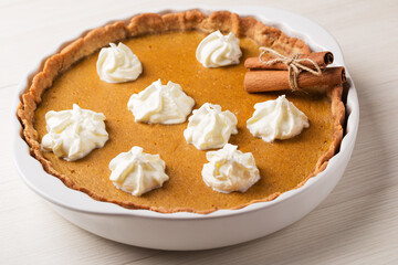 Freshly baked pumpkin pie with whipped cream, cinnamon sticks on rustic, white wood background. Harvest Festival, Happy Thanksgiving.