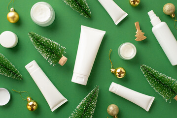 Winter season skin care concept. Top view photo of white tubes jars spray bottles gold baubles and christmas trees on isolated green background with blank space