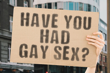 The question " Have you had gay sex? " is on a banner in men's hands with blurred background. Illegal. Love. Prohibit. Healthy. Adult. Immoral. Behavior. Bisexuality. Sensual. Affection. Desire