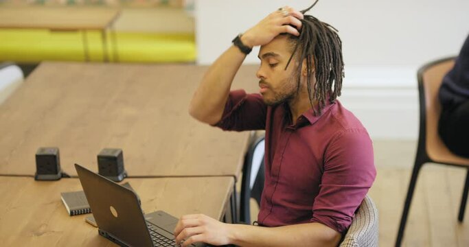 Man with dreadlocks using smart phone and laptop in office