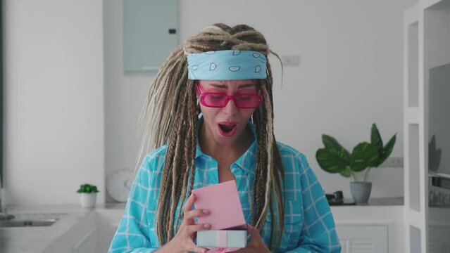 Emotional happy woman with dreadlocks and pink glasses enjoying gif, looking at box with excitement of modern kitchen background